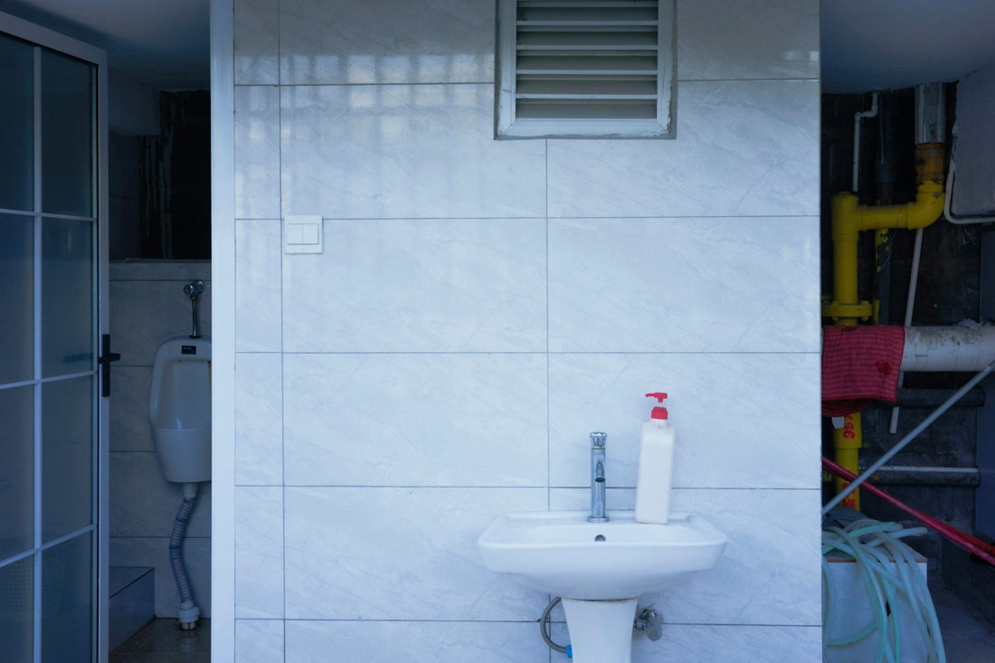 Tiled utility room with a white sink and exposed pipes.