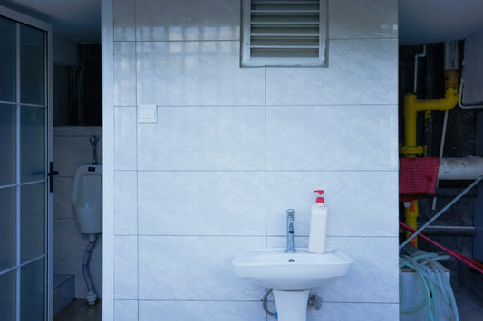 Tiled utility room with a white sink and exposed pipes.