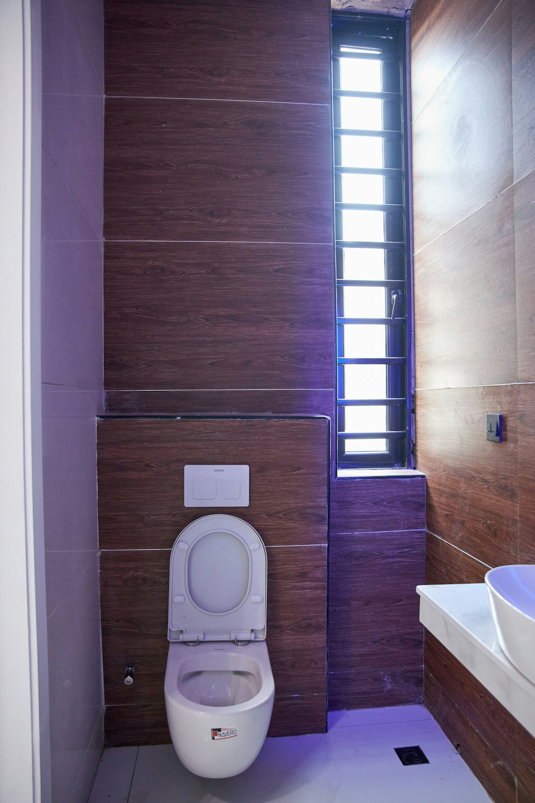 A modern bathroom with wood-look wall tiles, a white toilet, and a tall window