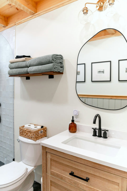 A bathroom with a wooden vanity, white sink, and an irregular mirror on a wall